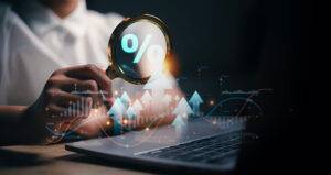 Financial analysis concept with a magnifying glass highlighting a percentage symbol over a laptop, surrounded by digital graphs and upward arrows indicating growth.